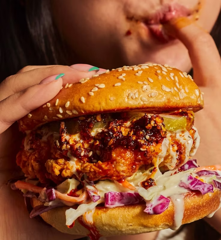 Person holding a crispy chicken burger with chilli oil, slaw and pickles